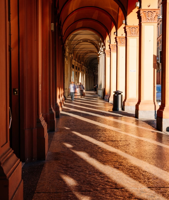Colonnato storico a Bologna con luce del sole che filtra tra gli archi.